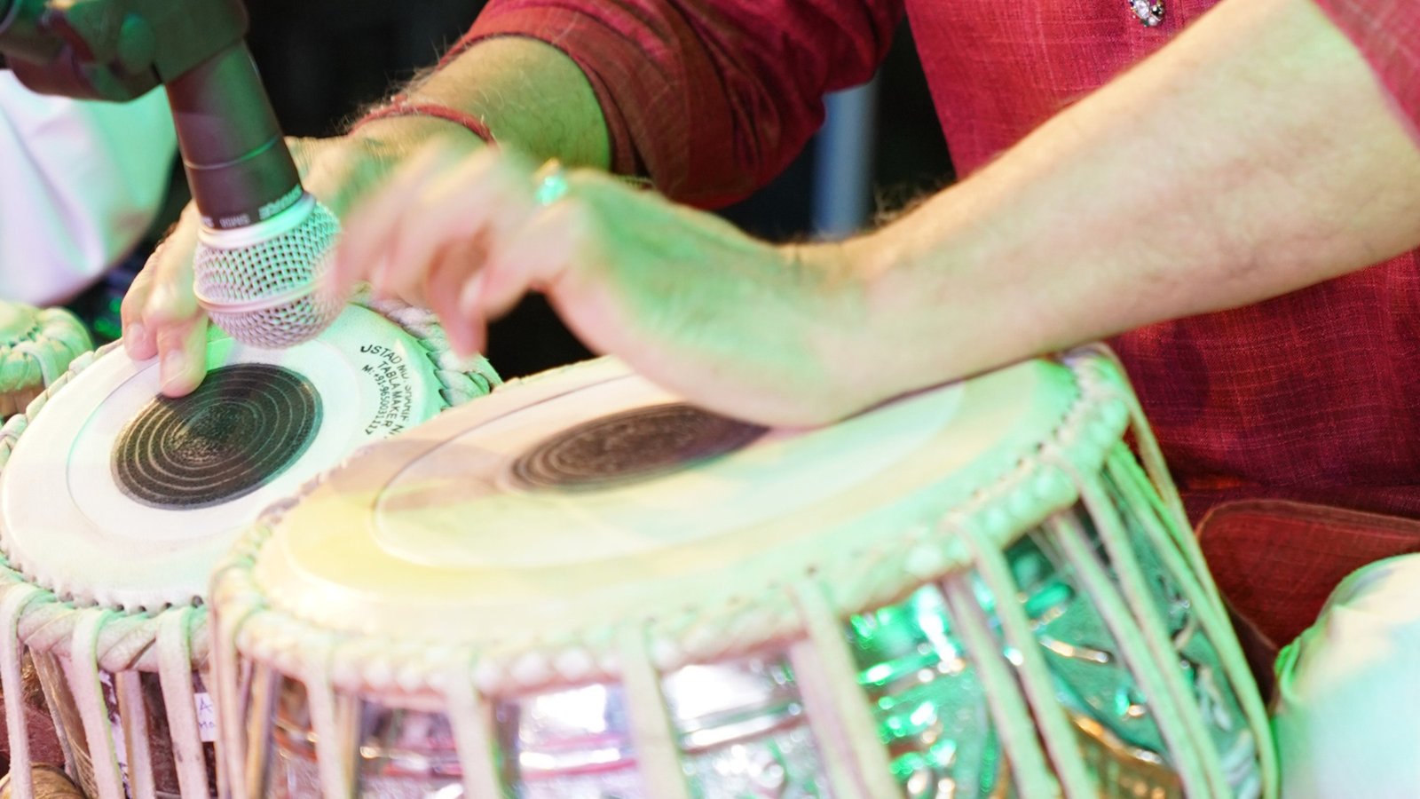 Hands mid-stroke on the tabla under green stage light